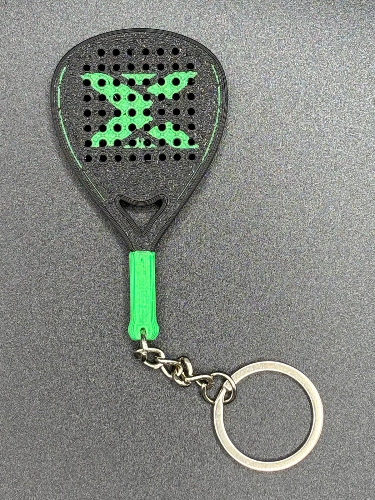 Llavero pala de pádel negro con la X y el puño en verde, cara perforada, cadena y anilla metálica