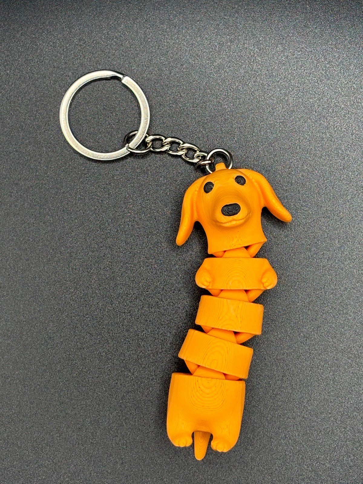 Llavero perro salchicha naranja con el cuerpo articulado por segmentos, con cadena y anilla metálica
